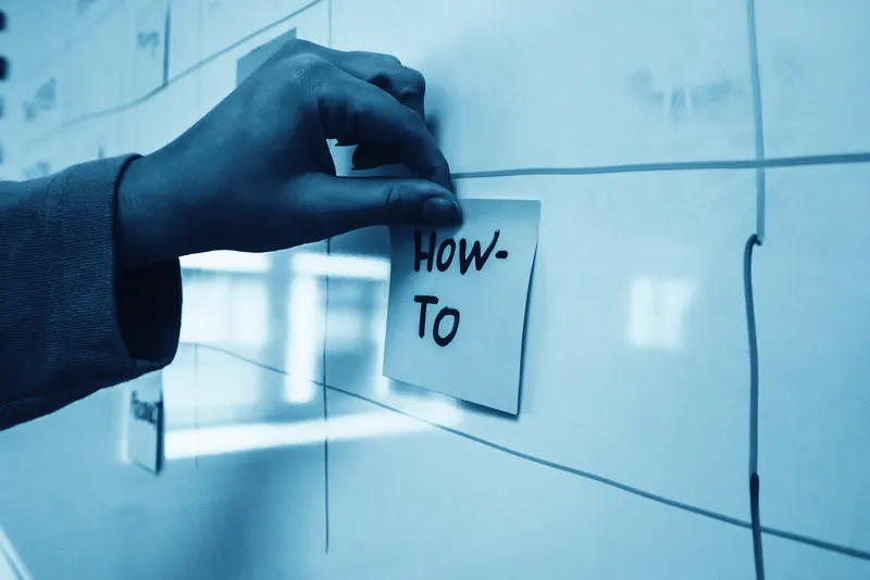 Une main colle un post-it sur un tableau de planification