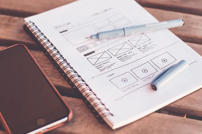 Carnet ouvert sur des croquis de wireframes, à côté d’un téléphone